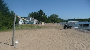 A sandy beach with a volleyball net, a boat, and a small building in the background.