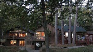 A two-story wooden cabin with a balcony, surrounded by trees.