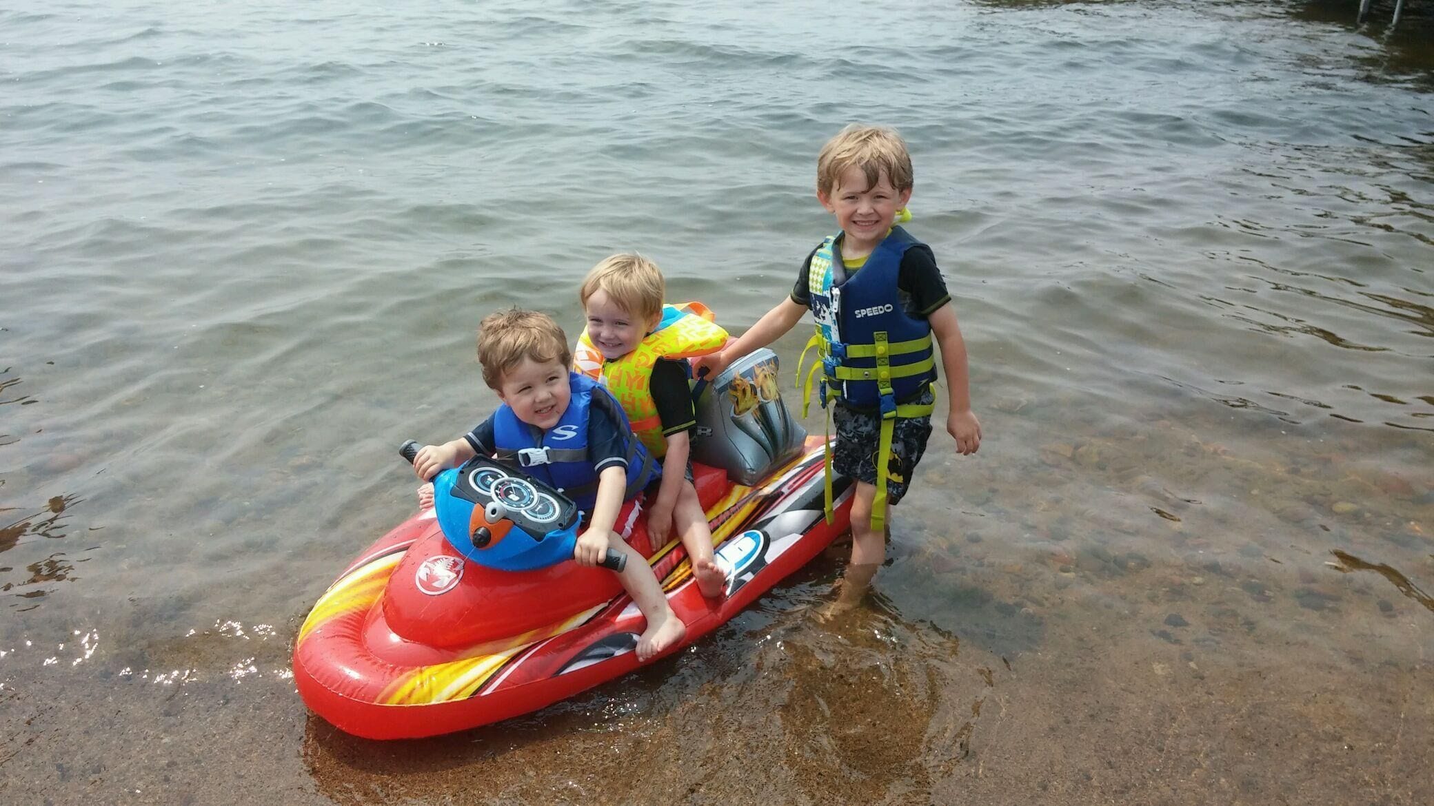 Tres niños en una embarcación hinchable roja en aguas poco profundas.