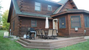 Una cabaña de troncos con un patio, mobiliario exterior y una parrilla.