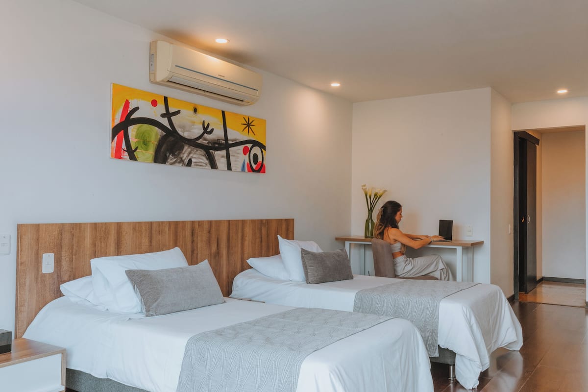 A hotel room with two beds, a desk, and an air conditioning unit.
