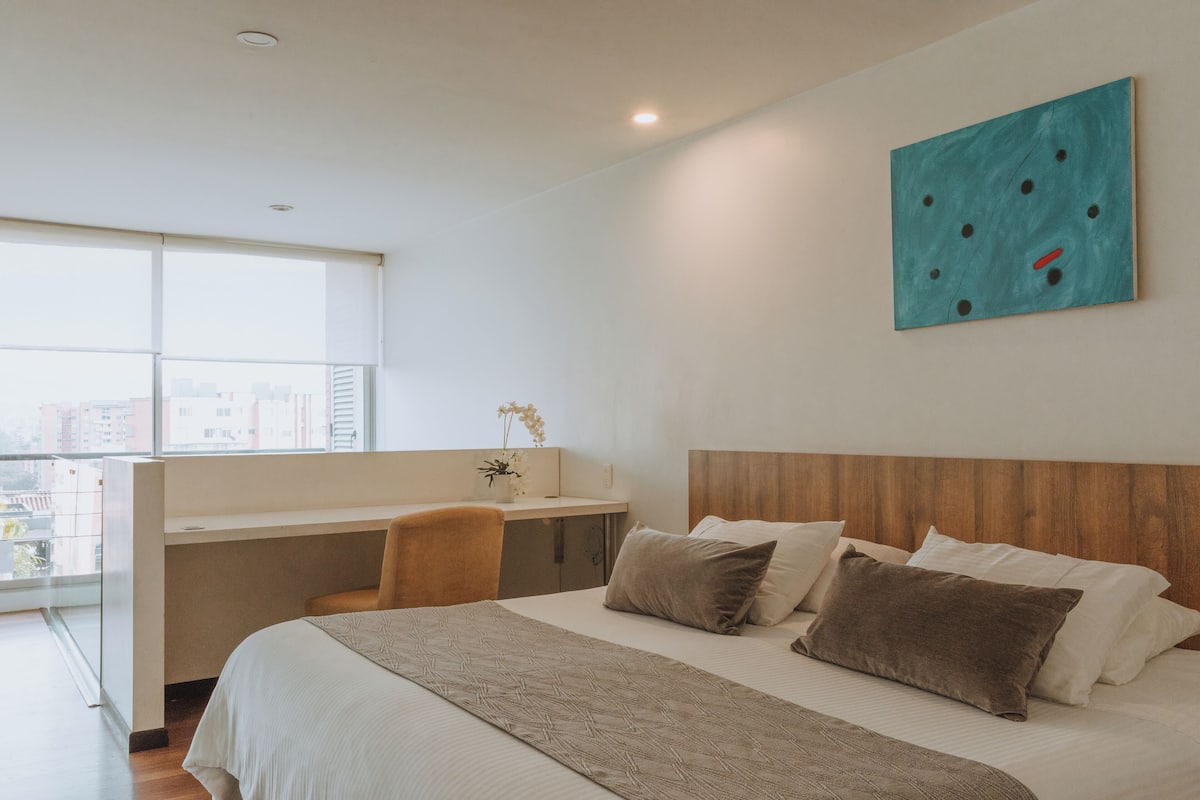 A modern hotel room with a large bed, a desk, and a city view.