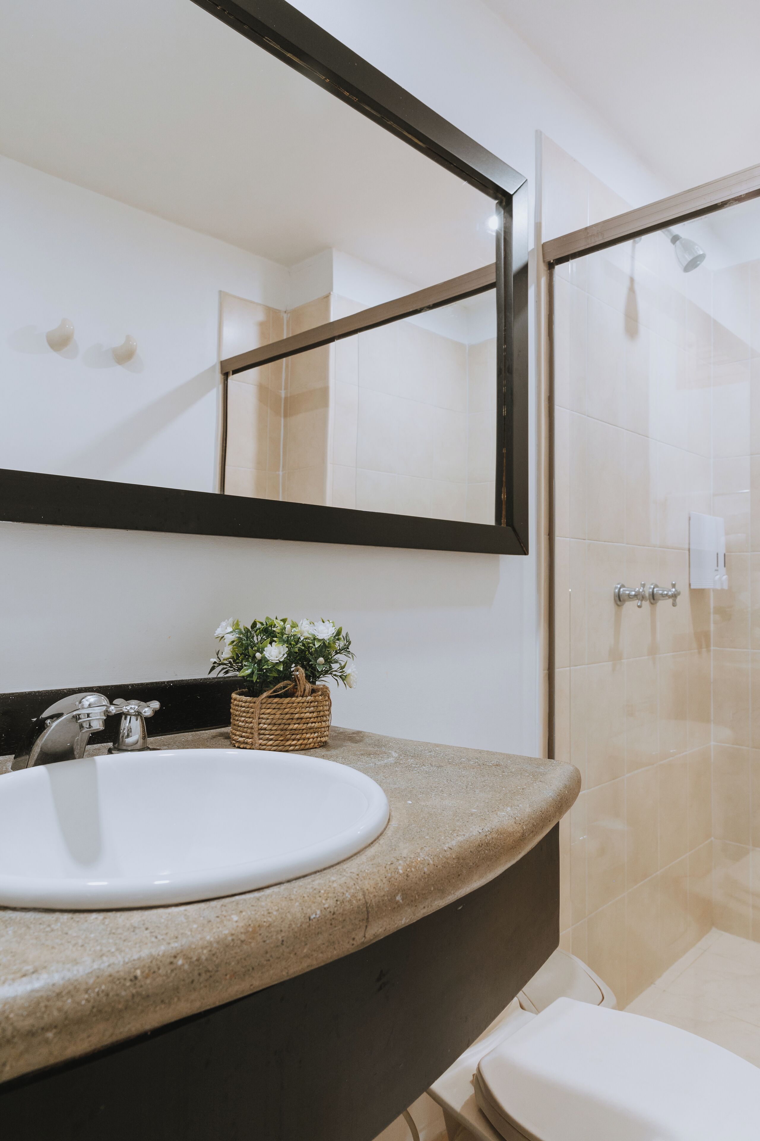 Un baño con lavamanos blanco, un espejo y zona de ducha.