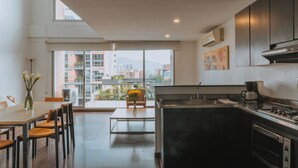 Uma cozinha moderna com uma janela grande, área de jantar com mesa e cadeiras, e vista para prédios lá fora.