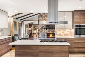 A modern kitchen with a central island, a stone accent wall, a built-in oven, and a fireplace.