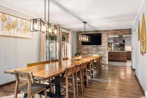 A modern dining area with a wooden table and chairs, a pendant light fixture, and a kitchen in the background.
