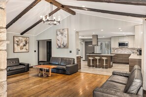 A spacious living area with a wooden floor, leather sofas, a coffee table, and a kitchen in the background.