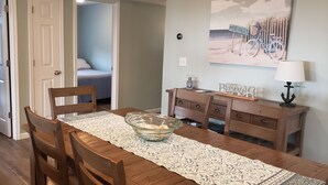 A dining area with a wooden table, chairs, a glass bowl, and a decorative wall piece. -  Penthouse Suite in the heart Sylvan Beach Resort (Sylvan Beach)