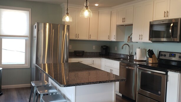 A modern kitchen with stainless steel appliances, a granite countertop, and bar stools. -  Penthouse Suite in the heart Sylvan Beach Resort (Sylvan Beach)