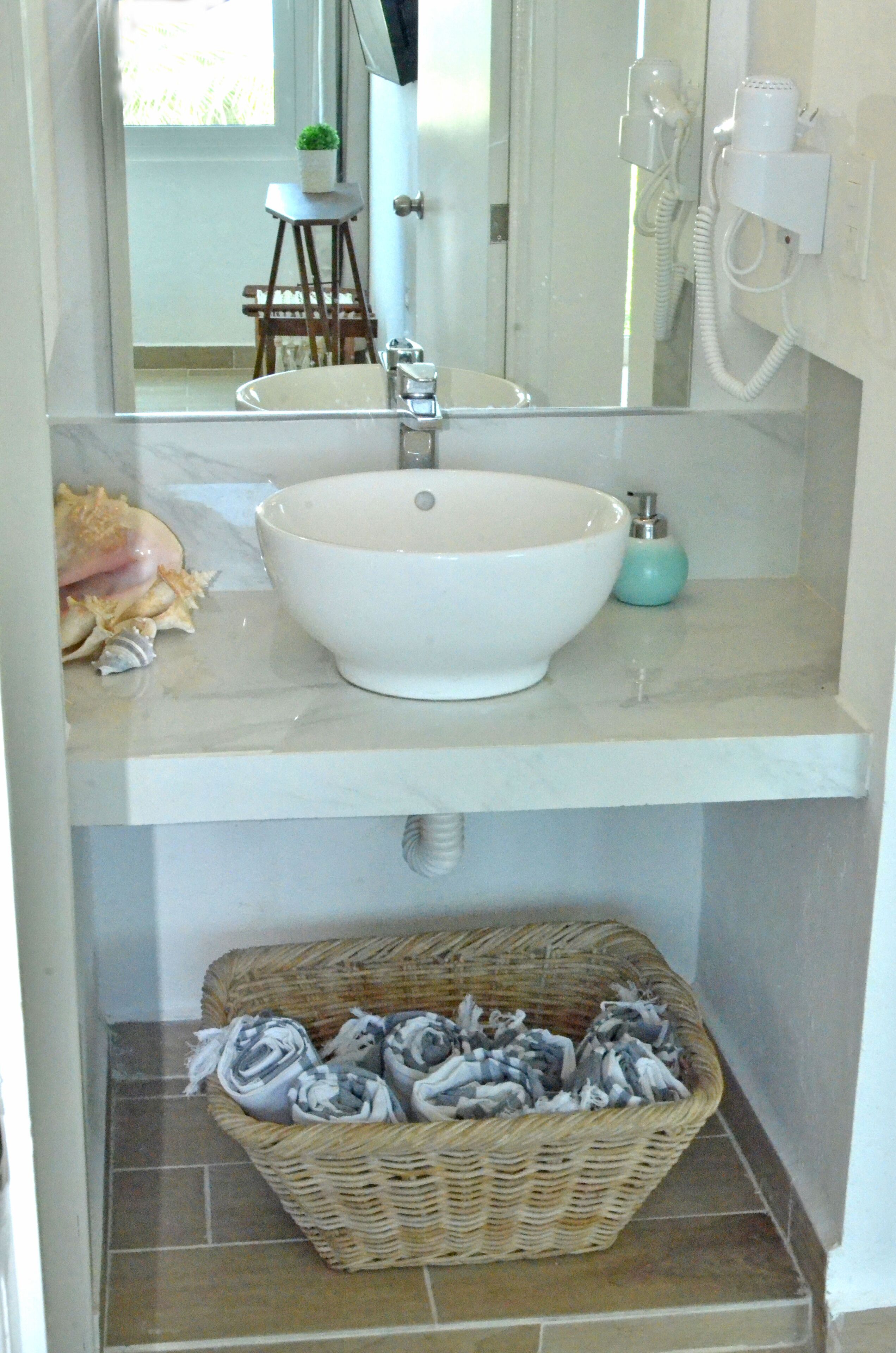 A bathroom with a white sink, a mirror, a small stool, and a wicker basket filled with towels.
