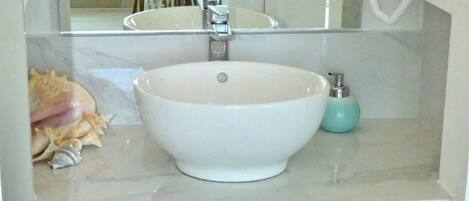 A bathroom with a white sink, a mirror, a small stool, and a wicker basket filled with towels.