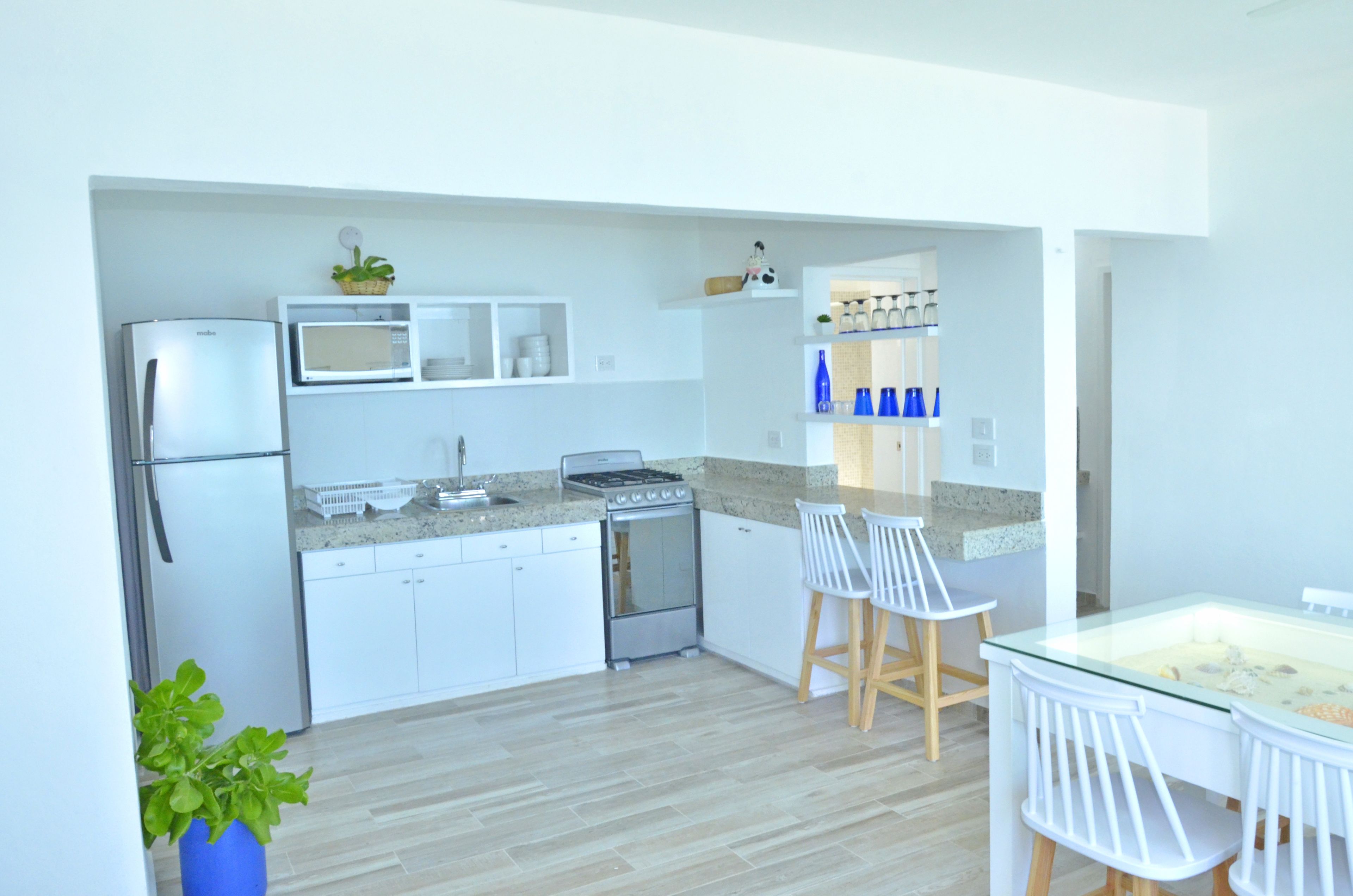 A modern kitchen with white cabinetry, a built-in microwave, a stove, and a dining area with white chairs and a glass table.