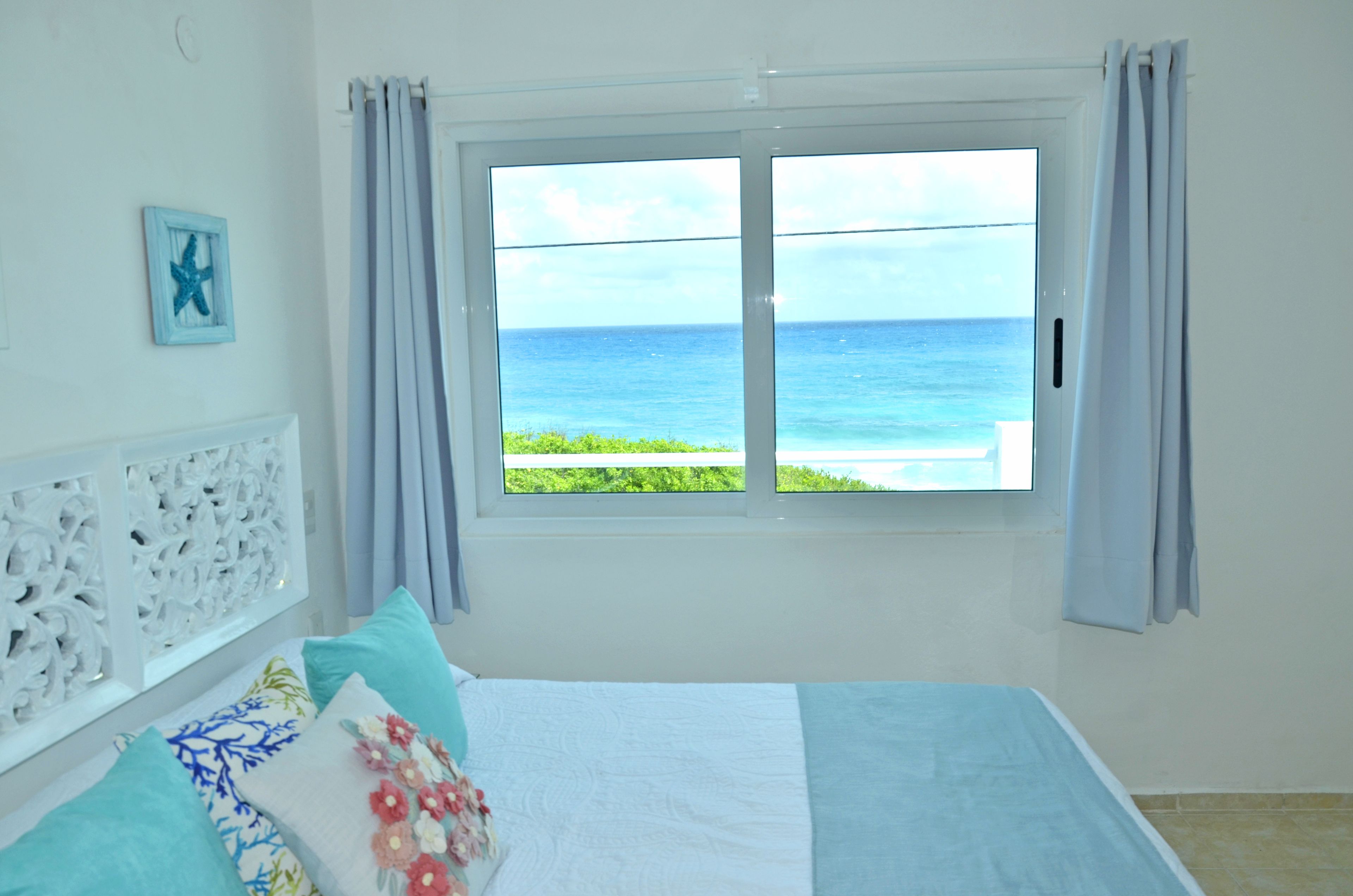 A bedroom with a bed, a window with curtains, a decorative wall panel, and a framed picture.