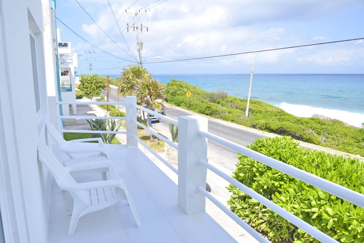 Un balcon avec des balustrades blanches donnant sur une route côtière et l’océan.