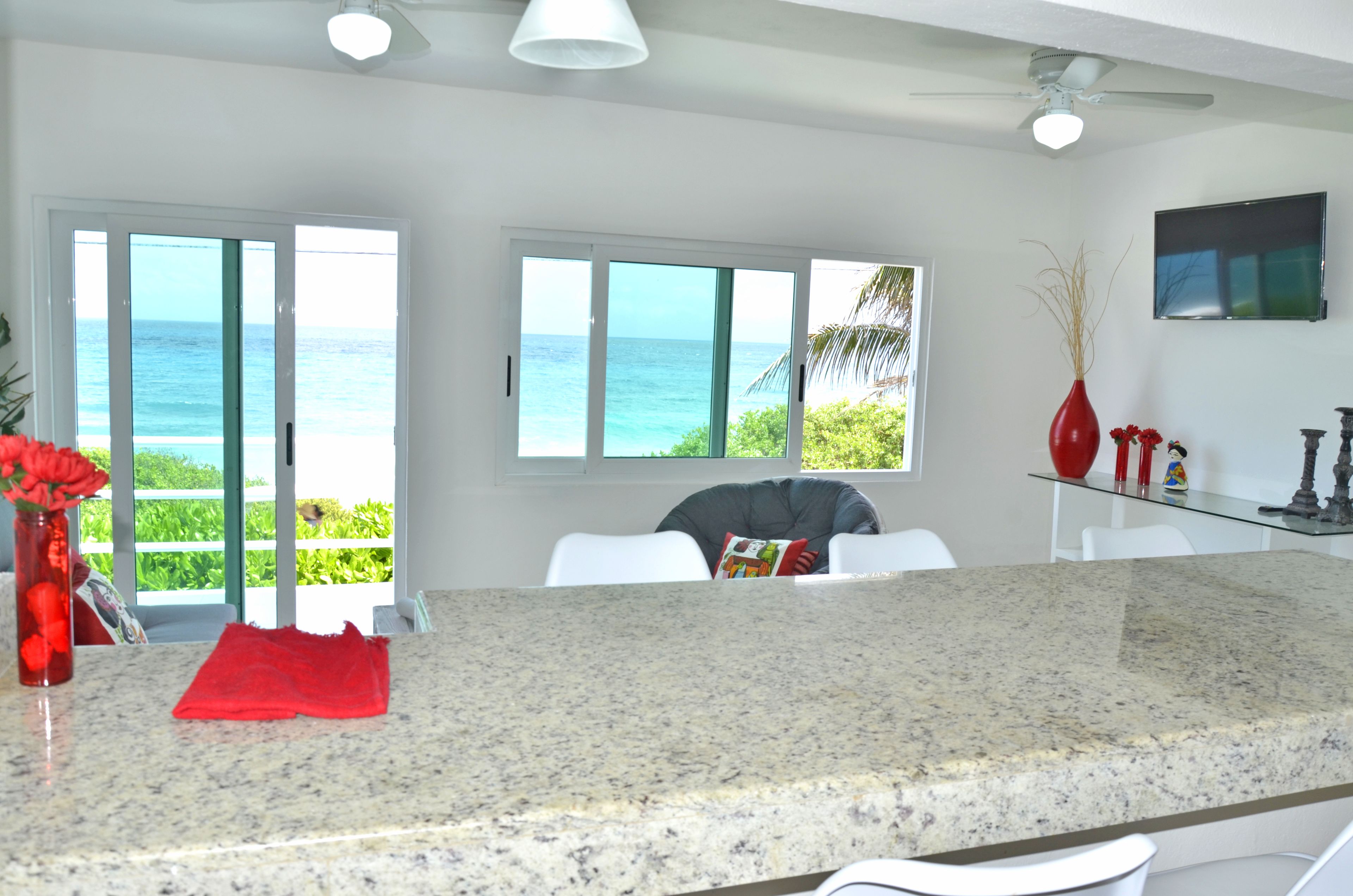 A kitchen with a granite countertop, a red vase, and a view of the ocean through large windows.