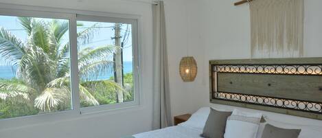 A bedroom with a large window, a bed with white and grey bedding, a wooden headboard, and a wall-mounted light fixture.