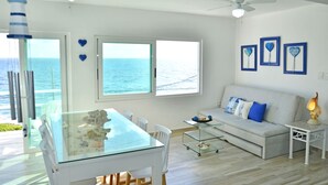 Una sala de estar moderna con una mesa de comedor de vidrio, sofá blanco y ventanas grandes con vista al mar.