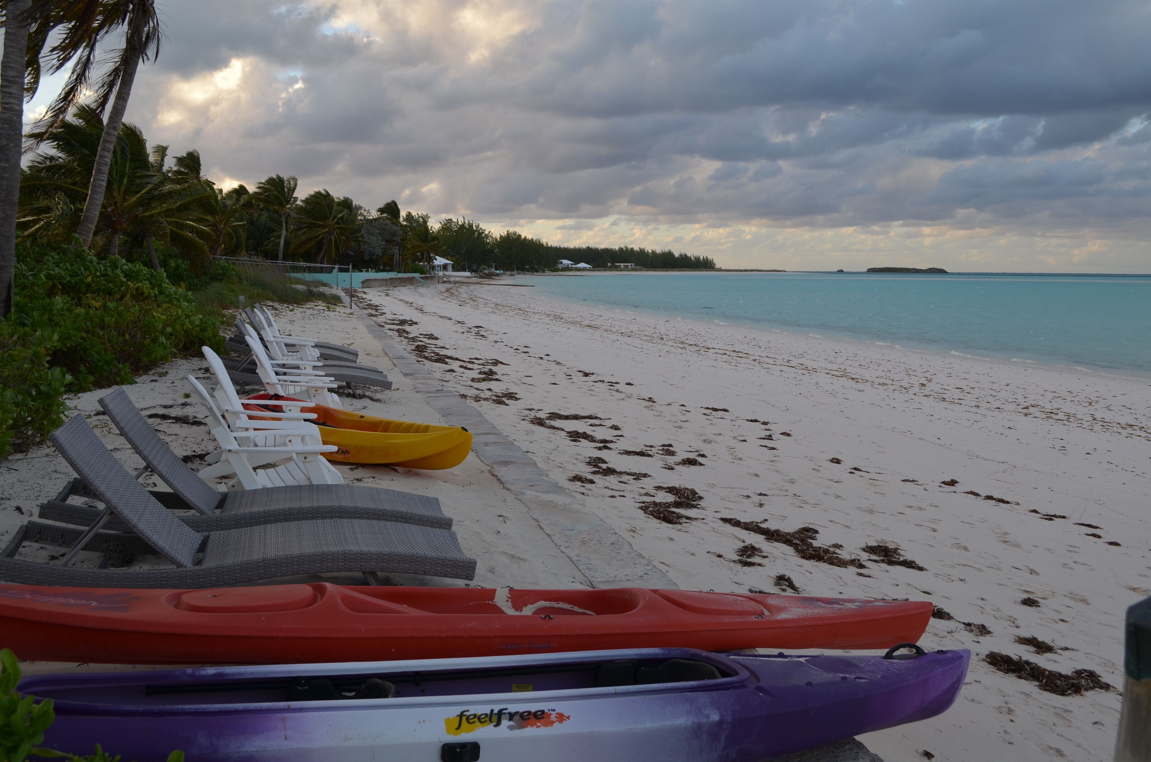 A beach with white sand and a row of lounge chairs along the shore.