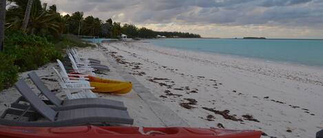 A beach with white sand and a row of lounge chairs along the shore.