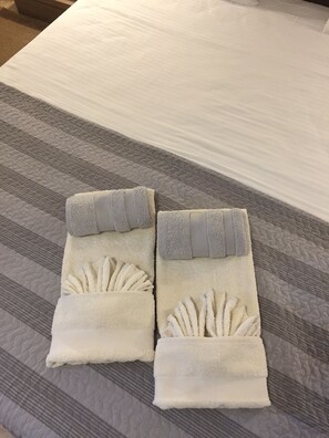 Una cama bien hecha con una colcha a rayas grises y blancas y dos toallas con diseño de concha dobladas en los extremos.