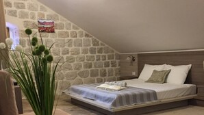 A bedroom with a stone wall, a bed with a wooden headboard, a bedside table, and a vase with green plants. - Studio apartment for couples (Kotor)