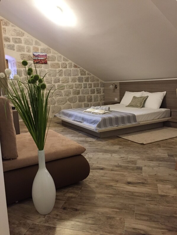 Un dormitorio con pared de piedra, cama con cabecera de madera, mesita de noche y un florero con plantas verdes.