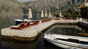 A marina with boats docked, lounge chairs, and umbrellas on a stone platform with a mountainous backdrop. - Studio apartment for couples (Kotor)
