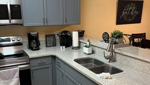 Una cocina con gabinetes grises, microondas, cafetera y un lavamanos.