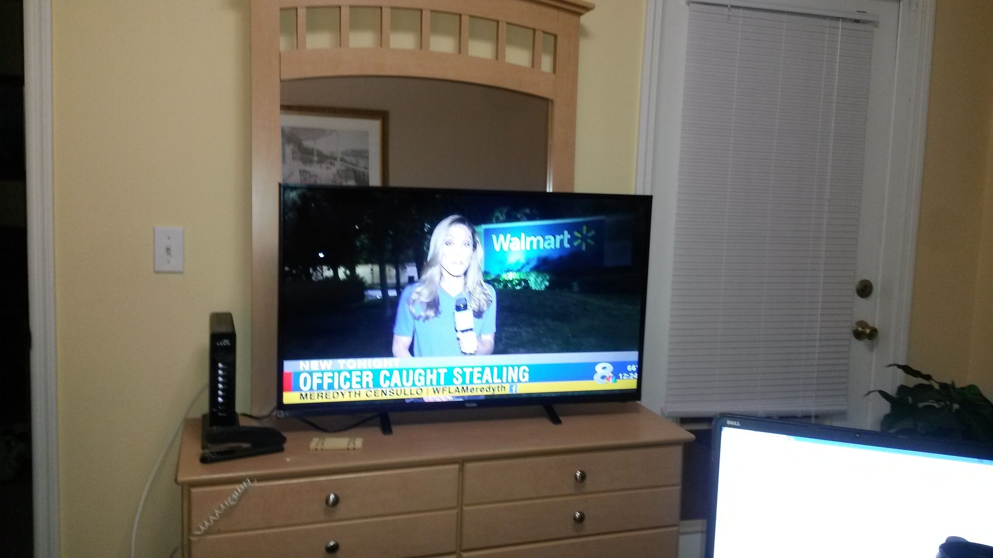 A television displaying a news broadcast with a caption "OFFICER CAUGHT STEALING" and a Walmart sign in the background.