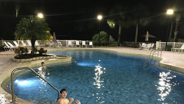 Una piscina con un letrero que indica una profundidad de 1 metro 18 centímetros, rodeada de sillas de descanso y palmeras.