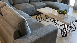 Una sala de estar moderna con un sofá seccional gris, una mesa de centro blanca con una planta y una lámpara de pie.