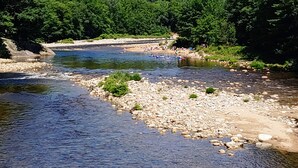 Ein Fluss mit steiniger Uferlinie und einer Brücke im Hintergrund.