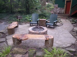 An outdoor seating area with Adirondack chairs, a fire pit, and wooden tables made from tree stumps. - Storybook Waterfront Cottage; Close to Hidden Valley/ Seven Springs (somerset)