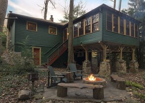 A two-story house with a stone foundation, green siding, and a fire pit in the backyard.
