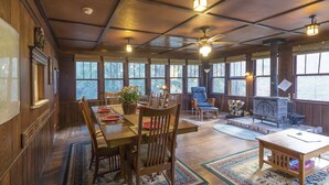 Un intérieur de chalet chaleureux avec un coin repas, des sièges, une cheminée et de grandes fenêtres.