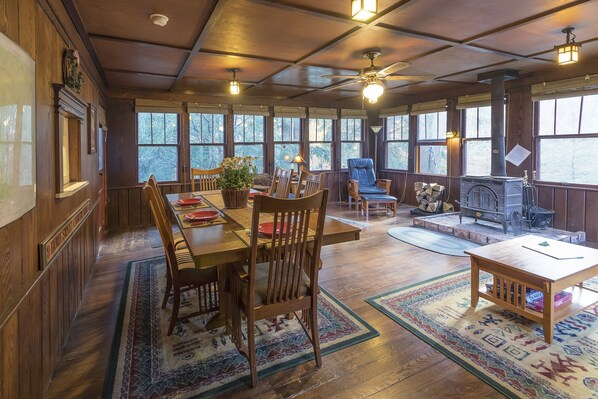 Interior acogedor de una cabaña con comedor, asientos, chimenea y ventanas amplias.