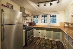 Una cocina con un refrigerador de acero inoxidable, estufa, microondas y un lavamanos. Hay ventanas con vistas a árboles.