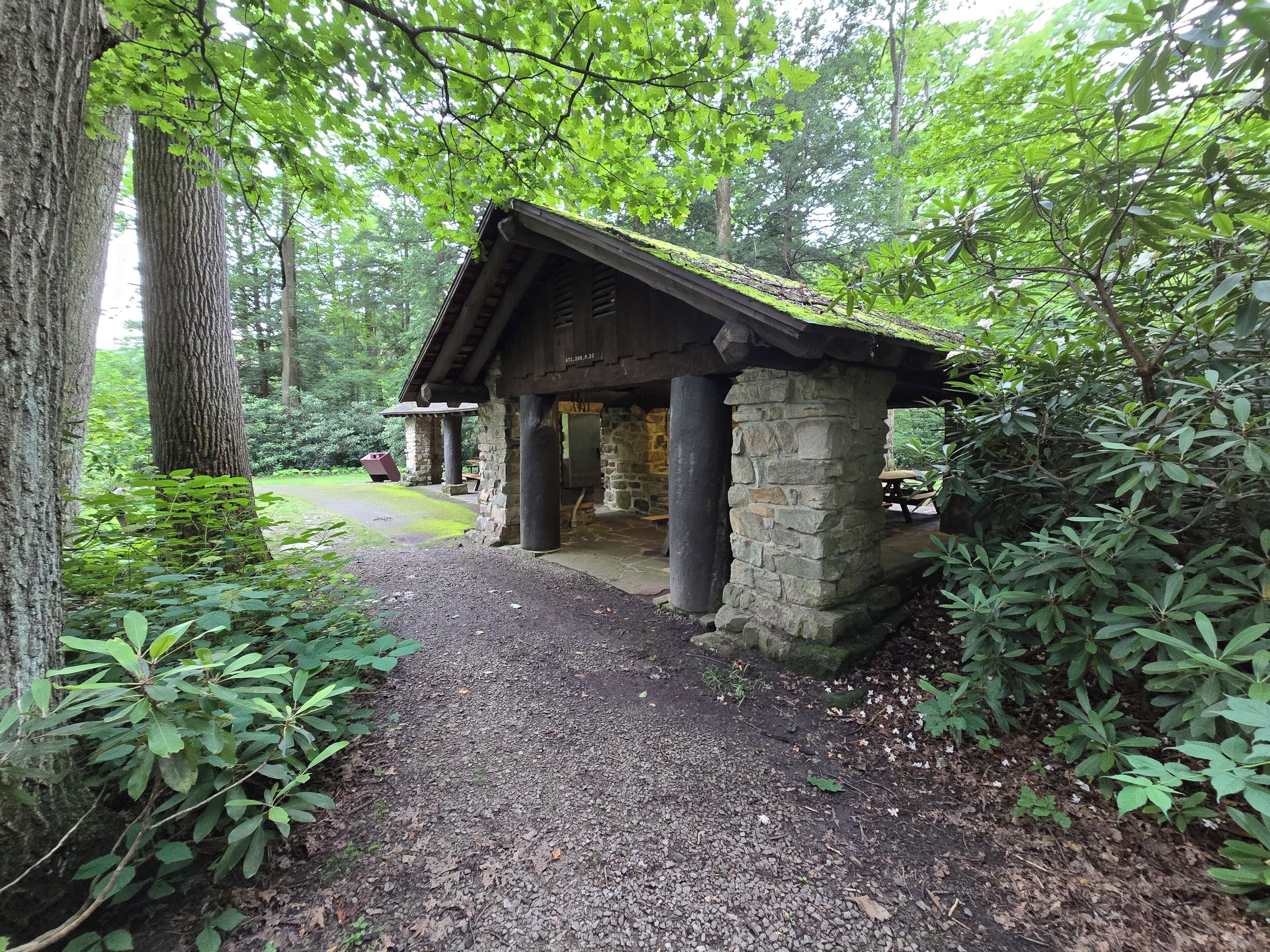 Un bâtiment rustique en pierre, doté d’un toit en bois, entouré d’une végétation luxuriante et d’arbres.