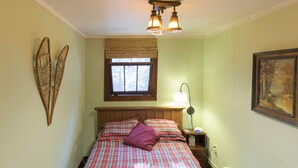Une chambre à coucher comprenant un lit, une table de chevet, une lampe, une fenêtre avec des stores et un élément de décoration murale.