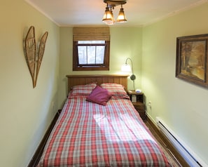Un dormitorio con cama, mesita de noche, lámpara, ventana con persianas y un adorno en la pared.