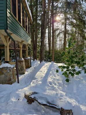 A wooden cabin with a porch, surrounded by snow-covered ground and tall trees.