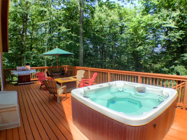 A wooden deck with a hot tub, outdoor furniture, and a grill.