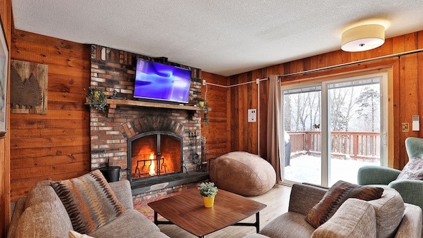 A cozy living room with a fireplace, a television, and a view of a snowy deck.