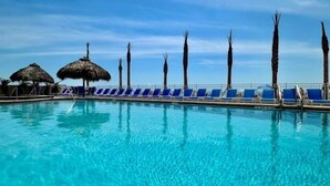 Una piscina azul cristalina con sillas de descanso y palmeras.