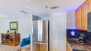 Una cocina con un refrigerador de acero inoxidable, armarios de madera, una encimera de mármol y un comedor con una silla azul.