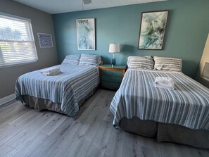A bedroom with two beds, a nightstand, a lamp, and artwork on the walls. - Best Sunsets on the Beach! 3/3 between Clearwater & St. Pete, Anglers Cove # 107 (Redington Shores)