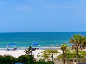A beach with clear blue water, a sandy shore, and a few umbrellas and chairs. - Best Sunsets on the Beach! 3/3 between Clearwater & St. Pete, Anglers Cove # 107 (Redington Shores)