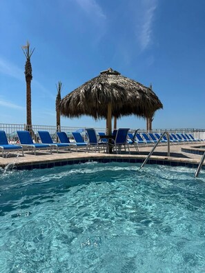 A pool area with blue lounge chairs and a thatched umbrella. - Best Sunsets on the Beach! 3/3 between Clearwater & St. Pete, Anglers Cove # 107 (Redington Shores)