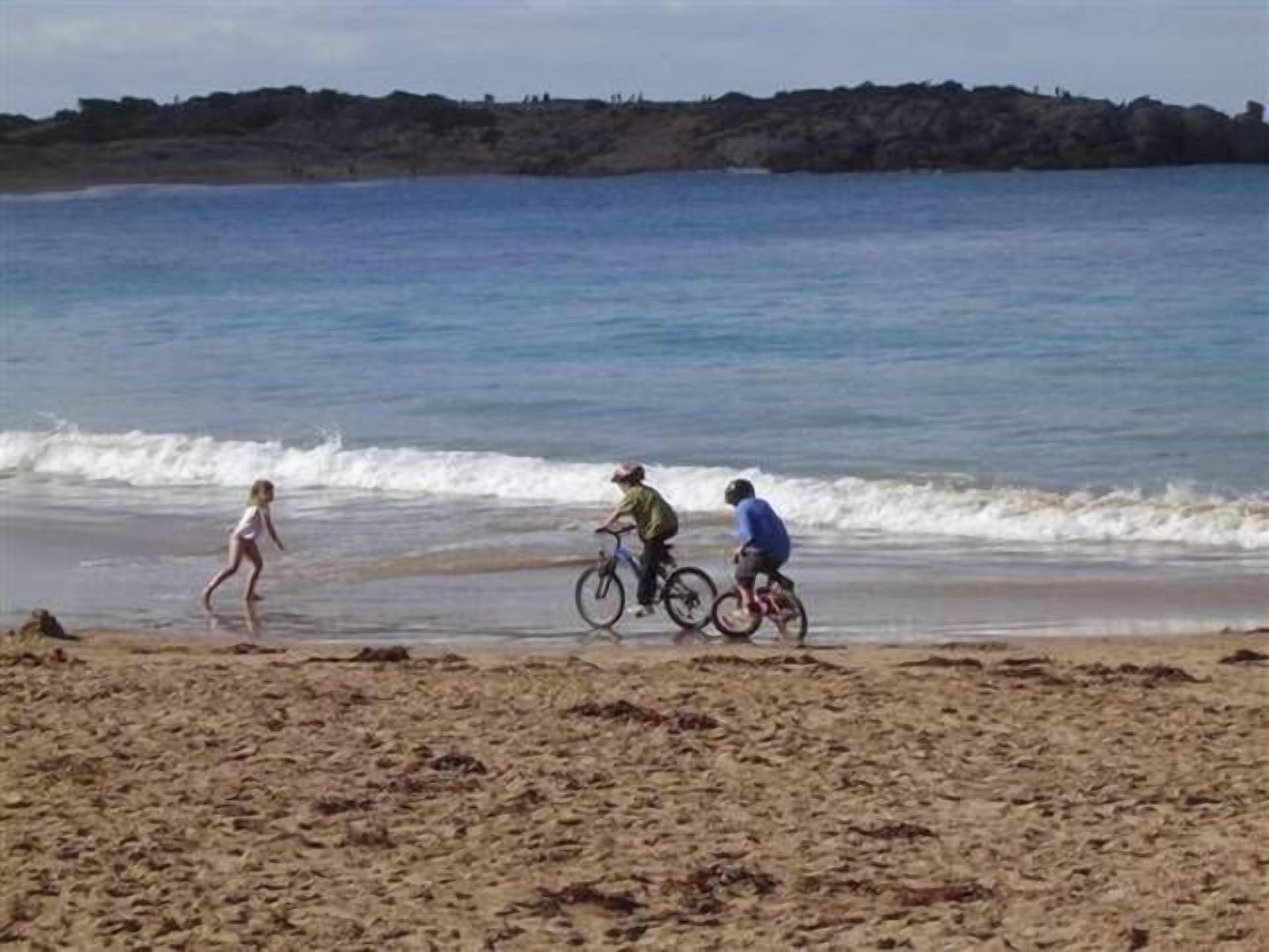 A beach with people walking and riding bicycles.