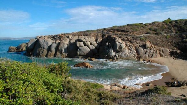 Eine Küstenlandschaft mit schroffen Klippen, einem Sandstrand und klarem, blauem Wasser.